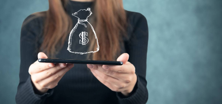 persona sosteniendo un smartphone de forma horizontal, del cual parece emerger una ilustración de una bolsa de dinero con el símbolo de dólar