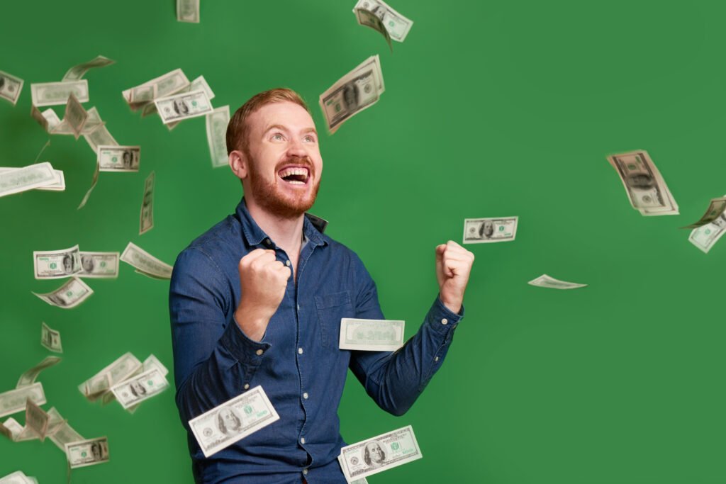 Un hombre pelirrojo celebrando eufórico con los puños cerrados mientras caen billetes de dólar a su alrededor