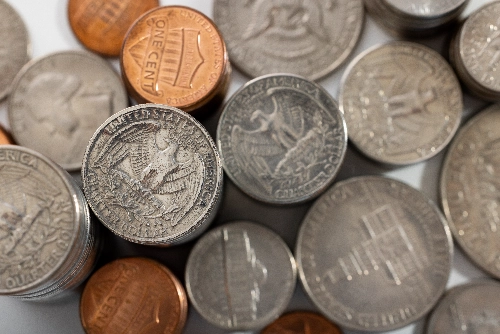 Varios fajos de billetes de cien dólares y pilas de monedas doradas sobre una mesa de madera oscura, con un fondo difuminado.