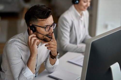 un agente de centro de llamadas con auriculares trabaja concentrado frente a la pantalla de su computadora en una oficina.