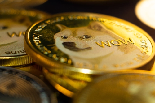Una moneda dorada de Dogecoin con la palabra "WOW" destaca en primer plano. Alrededor se aprecian otras monedas amontonadas y desenfocadas.