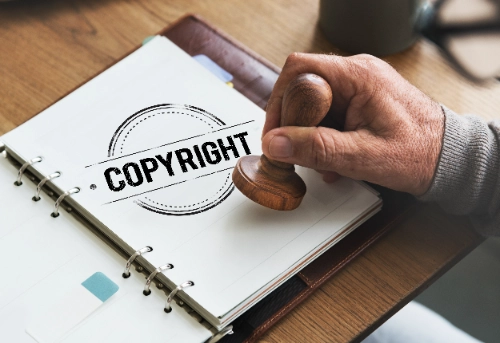 Una mano sostiene un sello de madera sobre una libreta abierta donde aparece estampada la palabra "COPYRIGHT".