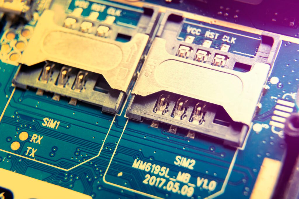 Placa de circuito impreso en primer plano que muestra dos ranuras para tarjetas SIM etiquetadas como SIM1 y SIM2 sobre una superficie metálica azul y amarilla.