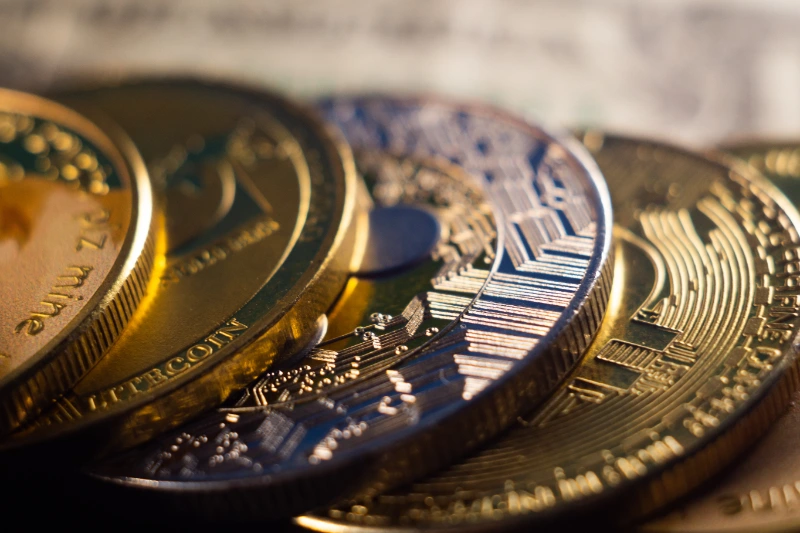 Un plano macro en ángulo bajo de monedas físicas de criptomonedas doradas y metálicas apiladas en fila con iluminación dramática y un fondo desenfocado.