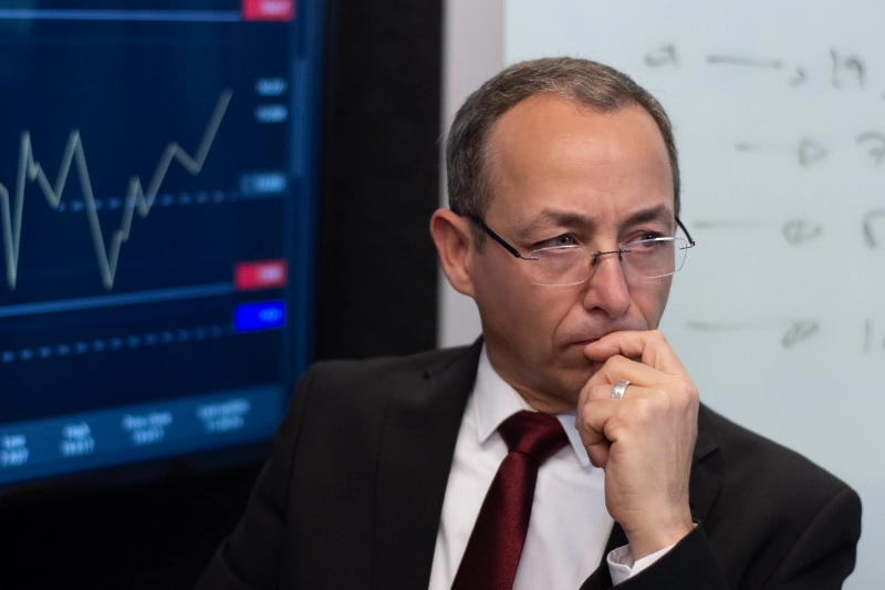 Retrato reflexivo de un analista financiero en traje evaluando gráficos bursátiles en una pantalla, representando la planificación estratégica y el análisis de mercados.